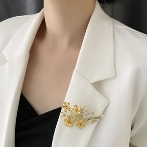 Elegant gold flower brooch with amber crystals and white stones pinned to a white blazer