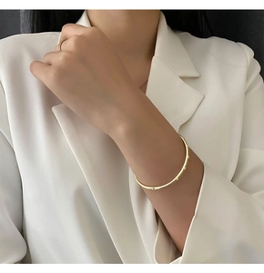 Detailed view of a gold textured cuff bracelet and minimalist ring on a model wrist