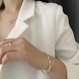 Elegant gold-tone zircon open bracelet and minimalist rings worn with a white suit