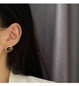 Detail of vintage gold-rimmed tiger eye stud earrings worn on a model side profile