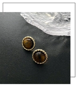 Macro shot of vintage tiger eye earrings with golden braided metal frames on ice base