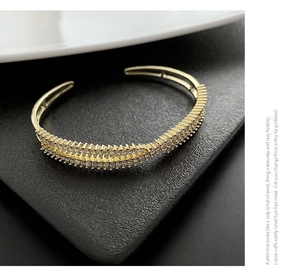 Detailed side view of golden crisscross bangle with micro-pave zircons on black surface