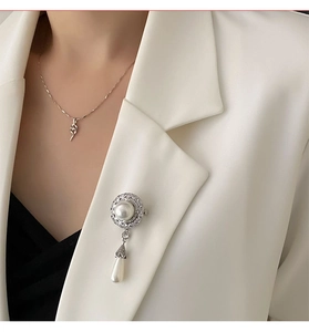 Detail einer eleganten Perlenbrosche mit Zirkonia-Besatz auf einem weißen Blazer
