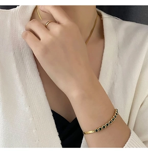 Detail of gold snake chain bracelet with green zircon stones on model wrist
