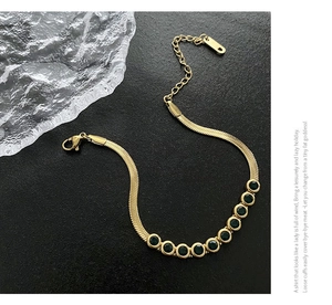 Detail of gold snake chain with green zircon gemstones on black leather background