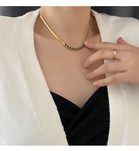 Close-up of gold necklace with green stones and matching ring on model's neck