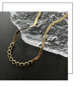 Detailed close-up of golden flat snake chain necklace with curved dark green zircon pendant