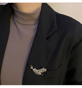 Detailed close-up of a golden wheat ear brooch with zircons on a black blazer lapel