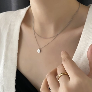 Double-layered silver necklace with round shell pendant shown on female model's neck