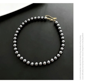 Vue macro d'un collier de perles métalliques sombres avec fermoir doré et chaînette