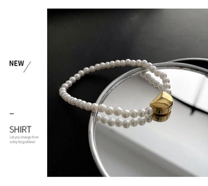 Detailed close-up of pearl bracelet with golden geometric clasp on reflective surface