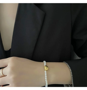 Elegant pearl bracelet with gold metal accent shown on wrist against a black blazer