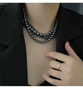 Gros plan d'un collier de perles noires multicouche sur col de veste avec bague en or