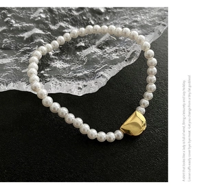 Detail view of pearl bracelet with polished gold geometric titanium steel charm on black surface