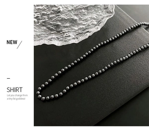 Détail d'un collier de perles noires polies sur fond mat avec texture de verre