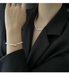 Close-up of minimalist pearl bracelet with golden pendant worn on black suit