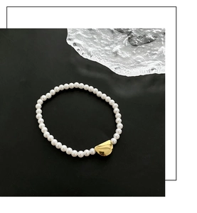 Detail of elegant faux pearl bracelet with a golden geometric bead on ice textured glass