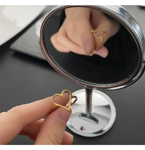 Vue détaillée d'une bague coeur dorée ajustable tenue à la main avec reflet miroir