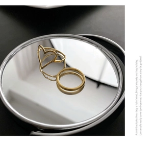 Détail d'une bague ouverte en cœur plaquée or et d'un anneau minimaliste sur un miroir