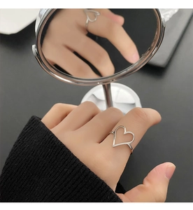 Gros plan d'une bague coeur argentée minimaliste portée au doigt avec reflet miroir