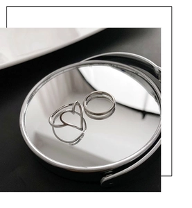 Bague coeur en argent poli et anneau fin présentés sur une surface de miroir ronde