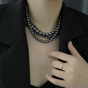 Collier de perles noires vintage à trois rangs porté avec un blazer et une bague en or