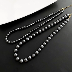 Trois tailles de colliers de perles gris foncé avec fermoir doré sur fond épuré
