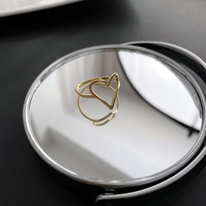 Bague cœur évidée dorée minimaliste au design ouvert sur une surface réfléchissante