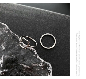 Macro shot of minimalist silver square geometric rings and thin metal bands on cool textured ice