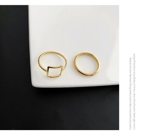 Detailed view of square geometric gold plated ring set on a white ceramic plate