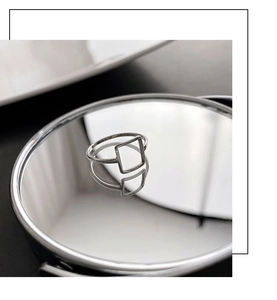 Detail of minimalist silver square open ring placed on a reflective mirror surface
