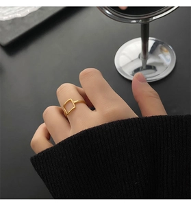 Minimalist gold square hollow ring shown on index finger with elegant dark knitwear
