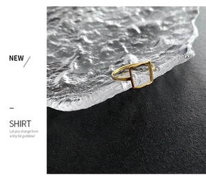 Detail of a gold square geometric ring on a wavy glass tray with a minimalist design