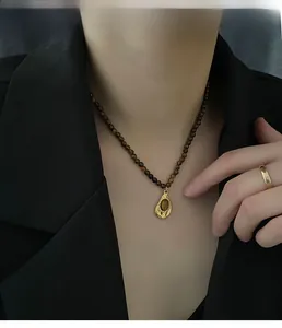 Gros plan sur un collier vintage en oeil de tigre et une bague dorée sur mannequin