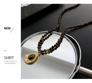 Détail d'un collier de perles en oeil de tigre avec pendentif doré en forme de goutte