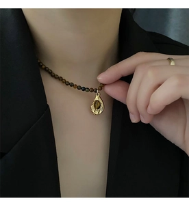 Détail d'un collier en perles d'oeil de tigre avec pendentif goutte doré sur veste noire