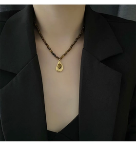 Détail du collier de perles en oeil de tigre avec pendentif goutte dorée sur un blazer