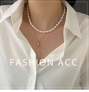 Detail of layered gold chain and pearl necklace set on white shirt background