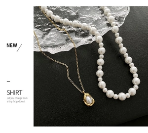 Detail of layered gold faux pearl necklaces with irregular textured charms on black surface