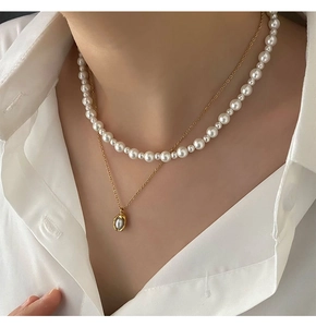 Detail of double-layered faux pearl necklace and gold chain with oval pendant on a model