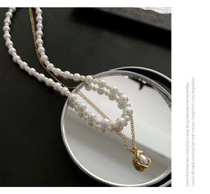 Detail of layered imitation pearl necklace with gold lava pendant on reflective surface