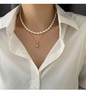 Detail of layered imitation pearl necklace with gold-rimmed pendant on a white shirt