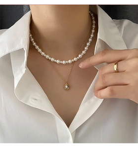 Detail of layered gold necklaces with white pearls and a matching ring on a model