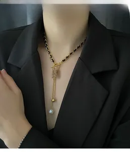 Detail of gold square plaque and pearl tassel on woven leather and steel chain necklace