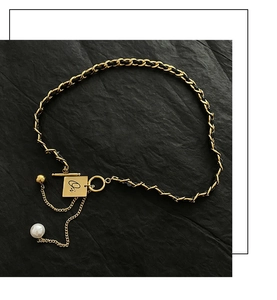 Detail of gold metal and black leather woven necklace with pearl charm and T-bar clasp