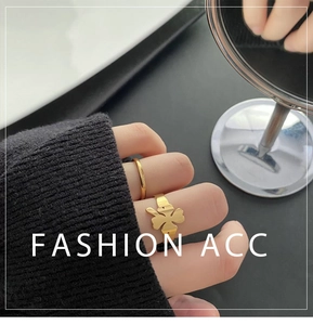 Close-up of a gold clover ring and a simple band worn by a model in a cozy setting