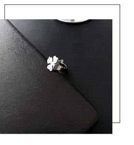 Macro detail of adjustable silver clover ring on a minimalist black textured background