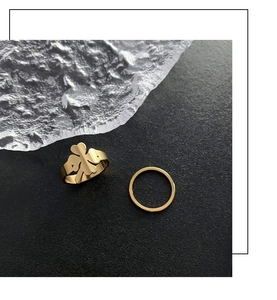 Detail of two-piece gold clover ring set on textured background with glass accents