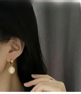 Detail of gold mother-of-pearl earrings and simple ring set on a model