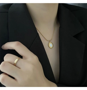 Close-up of a gold mother-of-pearl oval pendant necklace on a model wearing black